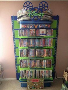 a green and blue book shelf filled with dvd's next to a pink wall