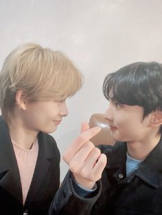 two young men standing next to each other eating doughnuts and looking at each other