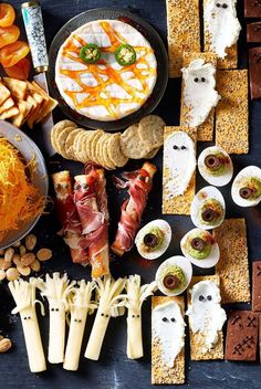 an assortment of appetizers and snacks are arranged on a black table with pumpkins