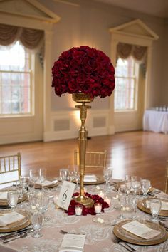 the centerpieces are adorned with red roses and gold chargers for an elegant touch