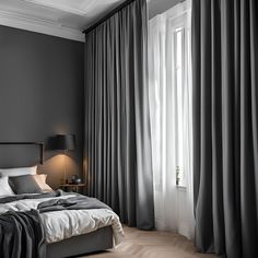 a bed sitting next to a window covered in gray curtained drapes on top of a wooden floor