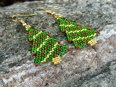 a pair of green and red beaded christmas tree earrings sitting on top of a rock