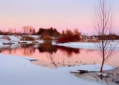 a river with snow on the ground and trees in the foreground, at sunset