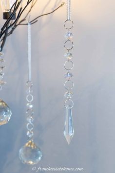 three glass ornaments hanging from a branch on a white wall with branches in the background