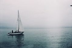 a sailboat in the ocean with two people on it and birds flying around them