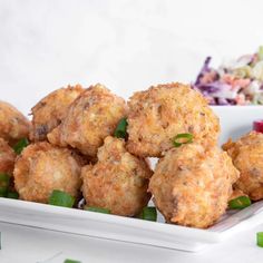 some fried food on a white plate with green onions and coleslaw in the background