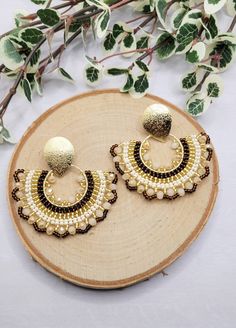 a pair of gold and black beaded hoop earrings on a wooden board with leaves