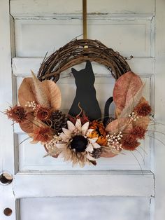 a wreath with leaves, flowers and a black cat on it hangs on the front door