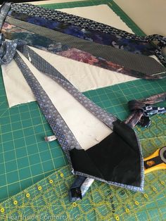 several ties laid out on top of a green cutting mat with scissors and other sewing supplies