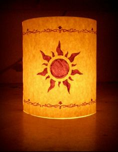 a paper lamp that is lit up with the sun in it's center and surrounded by ornate designs