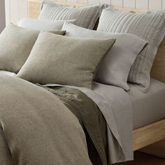 a bed that has some pillows on top of it and is made with grey linens