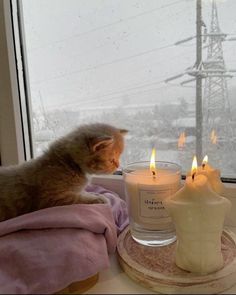 a cat sitting on a window sill next to two candles