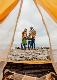 three people are standing in front of a tent on the beach with their hands together