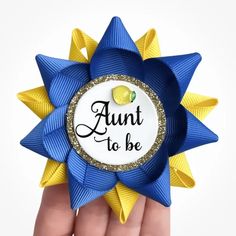 a hand holding a blue and yellow ribbon with the words, aunt to be on it