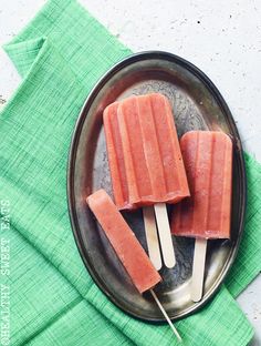 three popsicles sitting on top of a metal plate next to a green napkin and fork