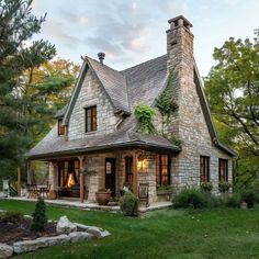 a stone house with a porch and windows on the front, surrounded by greenery