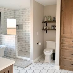 a white toilet sitting in a bathroom next to a walk in shower and wooden cabinets