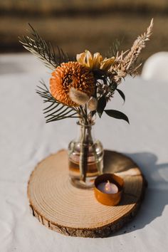 a vase filled with flowers sitting on top of a wooden slice next to a candle