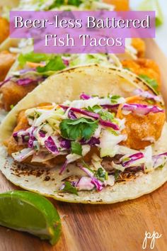 two fish tacos on a wooden cutting board with lime wedges next to them