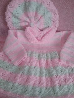 a pink and white crocheted baby sweater with hoodie on the top is laying on a bed