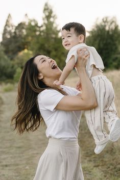 a woman holding a small child up to her face and smiling at the camera with trees in the background