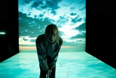 a woman standing in front of a large screen with the sky and clouds behind her