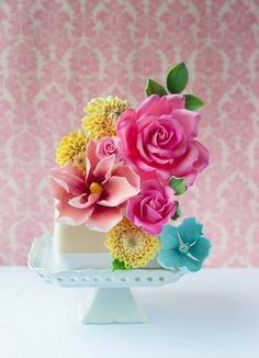 three pink and yellow flowers on top of a white cake