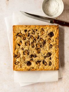 a square cake sitting on top of a white counter next to a knife and bowl