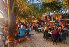 many people are sitting at tables on the beach