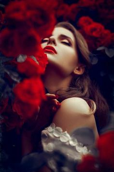 a woman with long hair and red lipstick is surrounded by roses in her hands, looking up at the sky