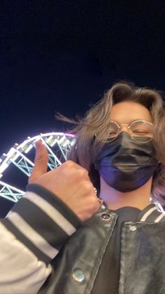 a person wearing a black mask and leather jacket with a ferris wheel in the background