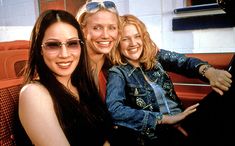 three women sitting next to each other on a red couch with their arms around one another