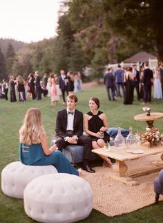 a group of people sitting on top of a grass covered field next to each other