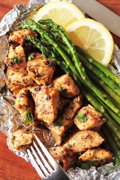 grilled chicken and asparagus on tinfoil with lemon wedges