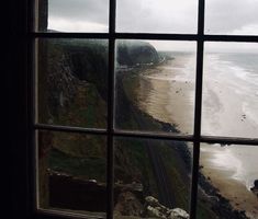 the view from an open window looking out at a beach and ocean with waves coming in