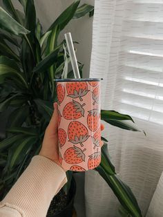 a person holding up a cup with strawberries on it in front of a potted plant