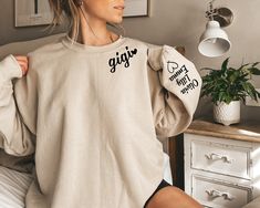 a woman sitting on top of a bed wearing a white sweatshirt with the word gigigi printed on it