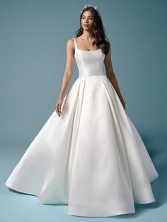 a woman in a white wedding dress with a tiara on her head, standing against a blue background