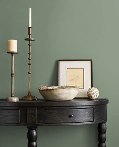 a wooden table with two candles and a bowl on it next to a candle holder