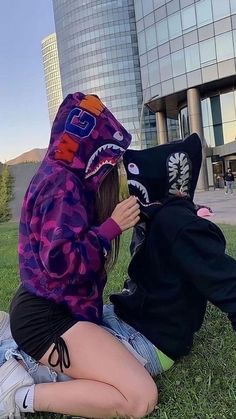 two people sitting on the grass in front of a building with a shark hoodie