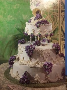 a three tiered cake with purple flowers on the side and an angel topper