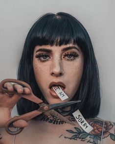 a woman with tattoos holding scissors in front of her face