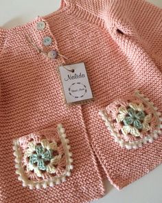 a pink knitted sweater with crochet flowers on the front and two buttons at the back