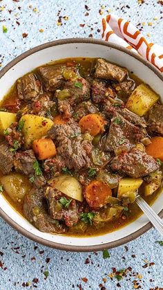 a bowl filled with stew and potatoes on top of a blue table cloth next to a spoon