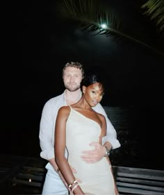 a man and woman standing next to each other in front of the ocean at night