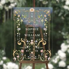 an easel with a wedding sign on it in front of some flowers and trees