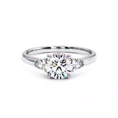 a white gold engagement ring with three stones on the side and a round brilliant diamond center