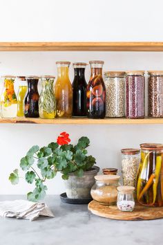 many jars are lined up on a shelf with flowers and herbs in them, along with other items