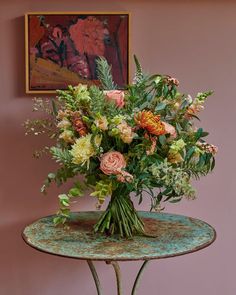 a bouquet of flowers sitting on top of a table next to a painting and chair