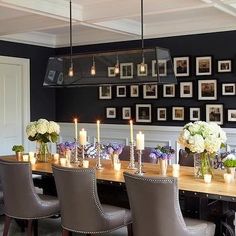 a dining room table with candles and pictures on the wall behind it, surrounded by gray upholstered chairs